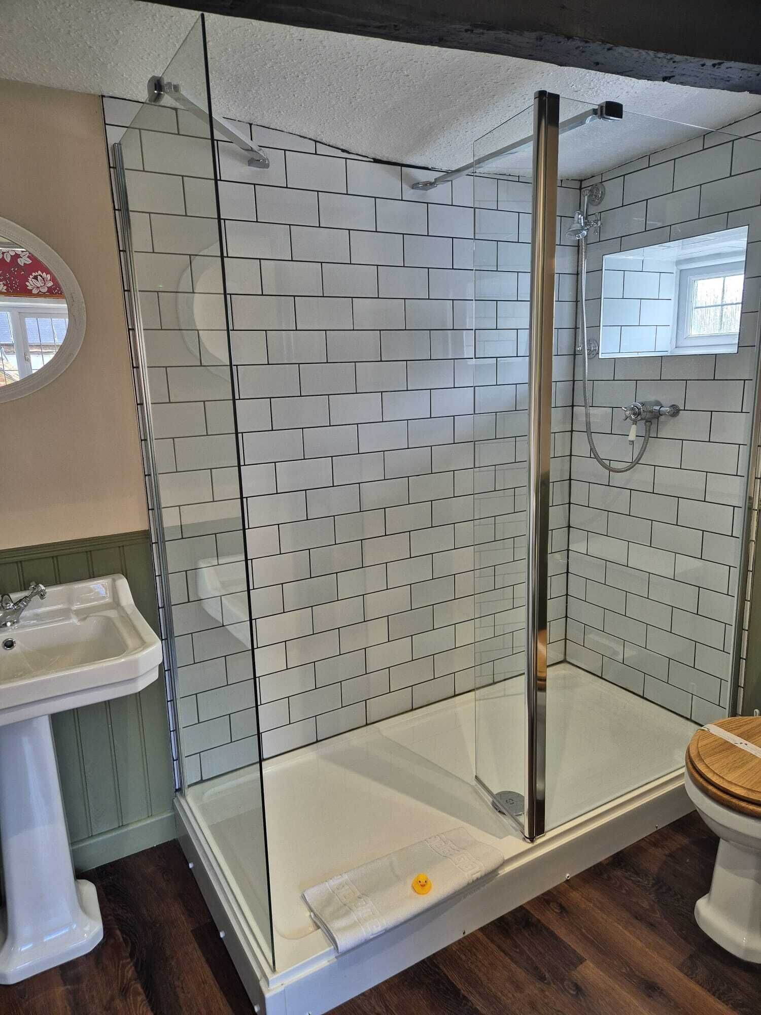Un baño con ducha de vidrio, lavamanos blanco y retrete.