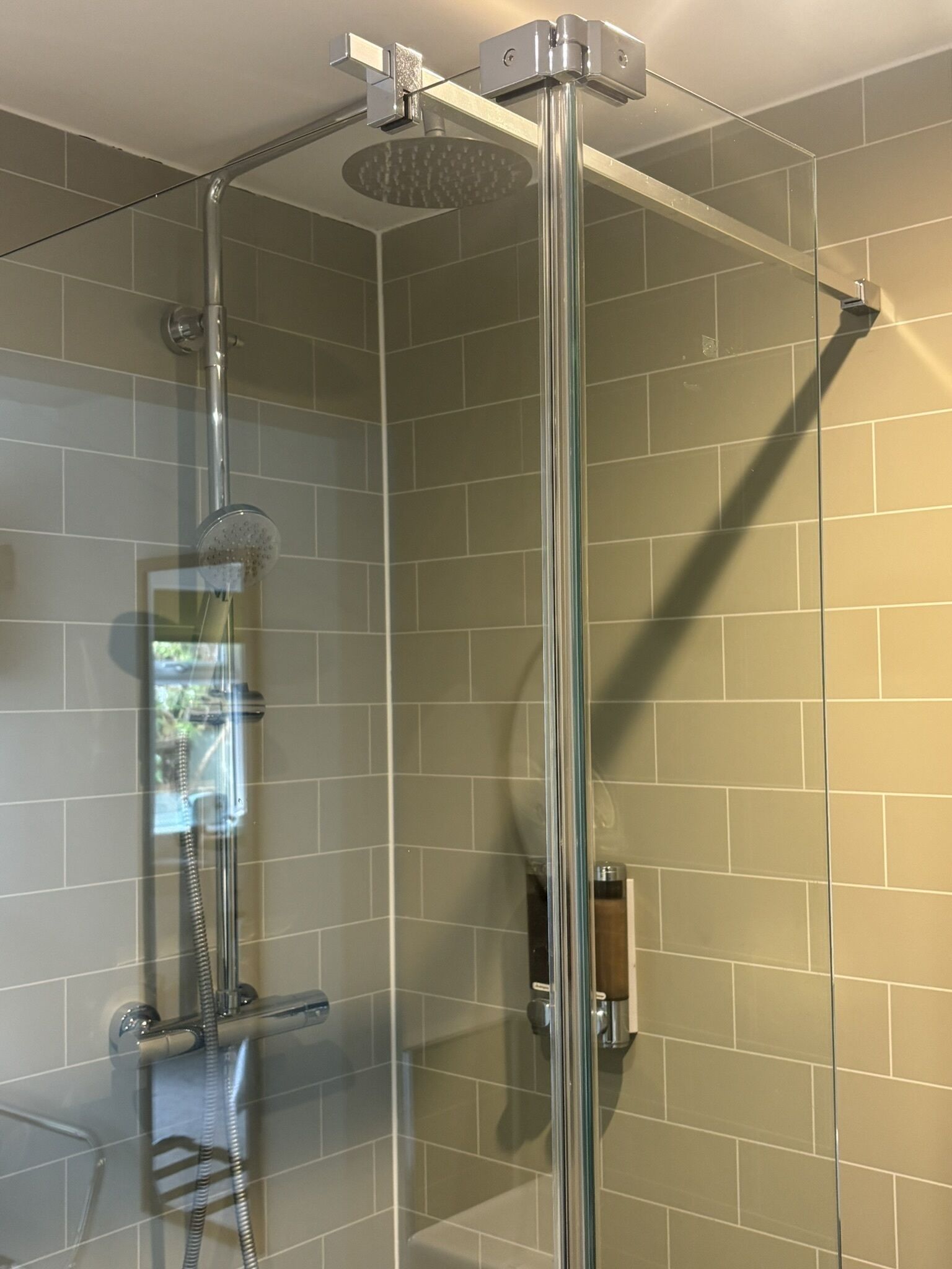 Et brusebad med glasvægge, en håndholdt brusehoved og et kontrolpanel på væggen.