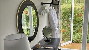 Une chambre d’hôtel avec un bureau noir, un miroir, une lampe, une télécommande et une vue sur un jardin, visible à travers la porte.
