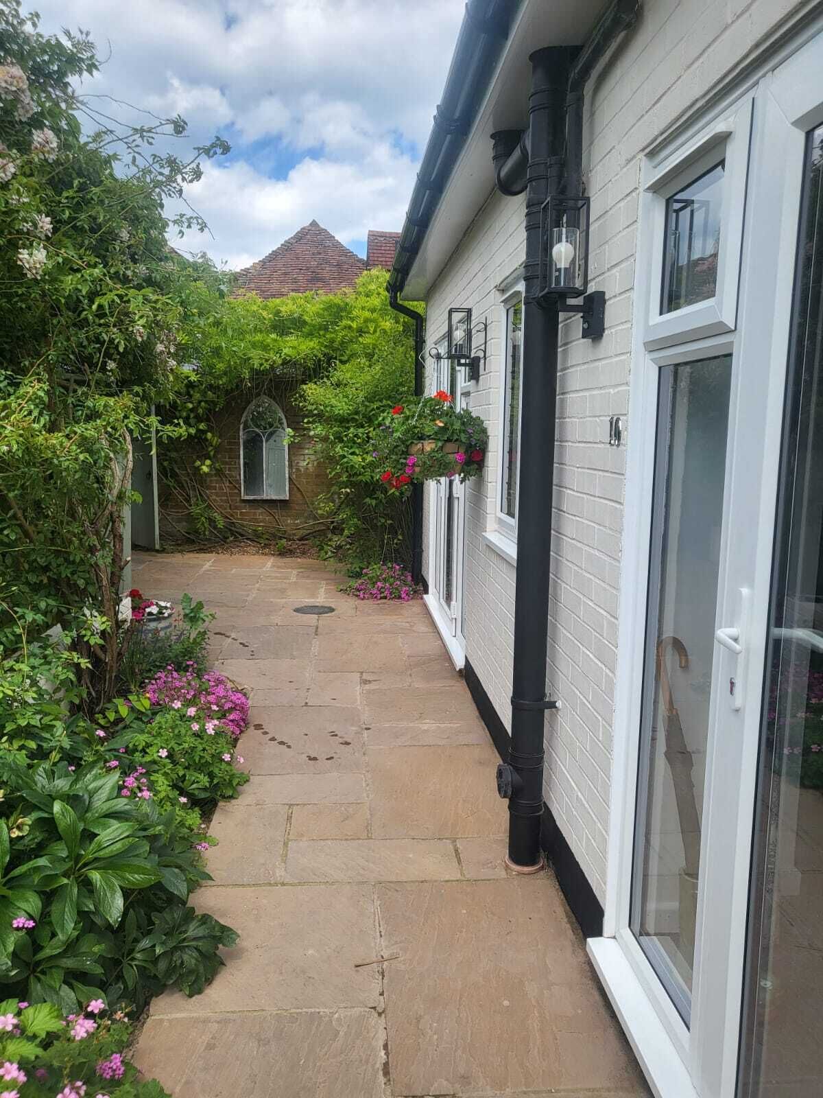 A narrow stone pathway leading to a white building with large windows and a brick chimney.
