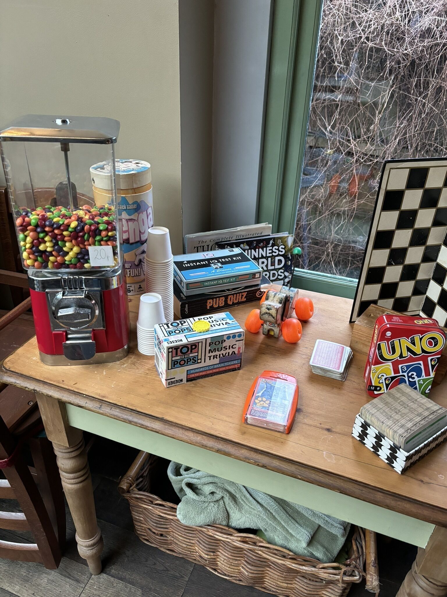 Una mesa con juegos de mesa, una máquina de dulces y una ventana con vistas a árboles.