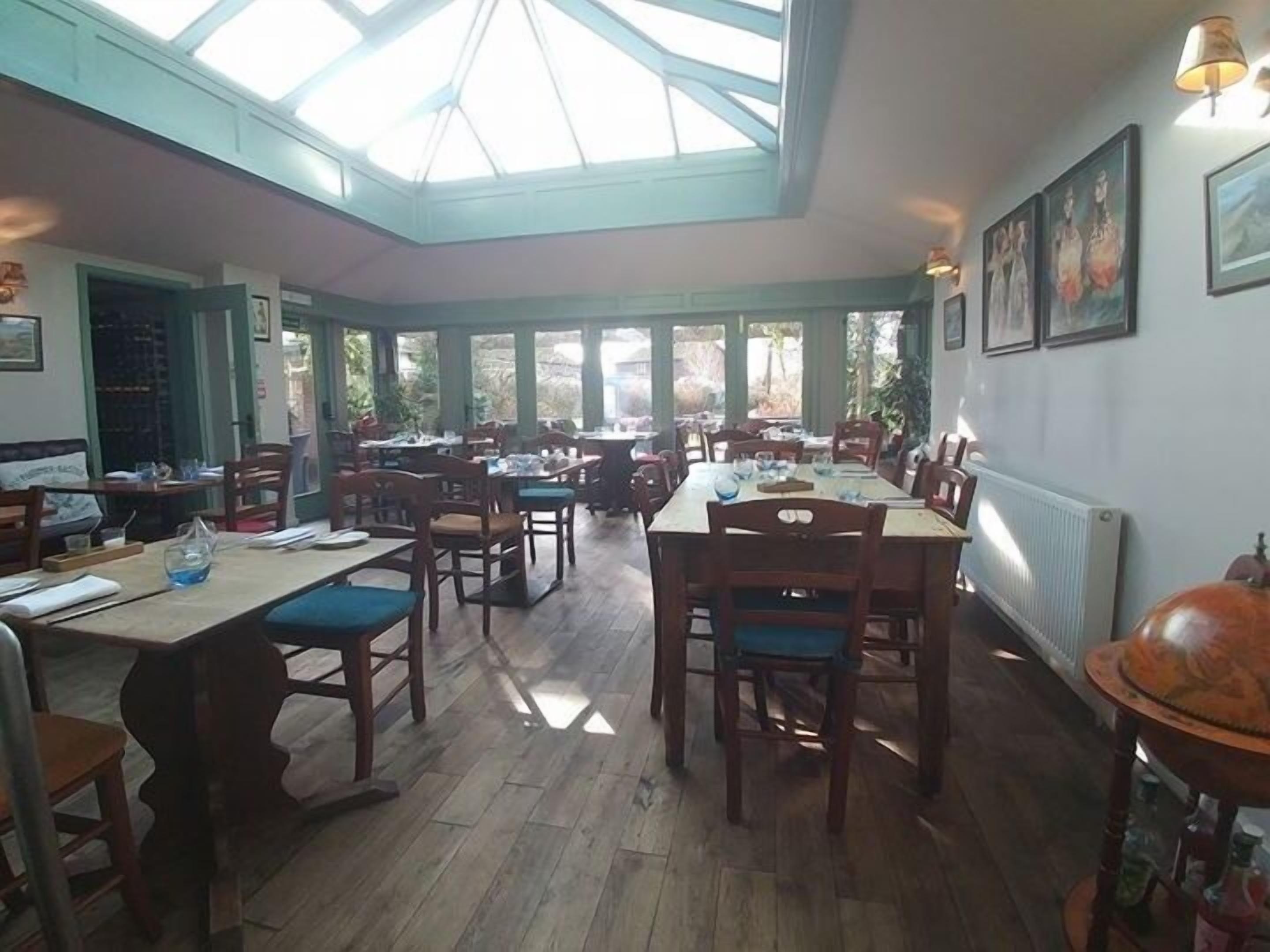 A restaurant with wooden tables and chairs, a skylight, and framed artwork on the walls.