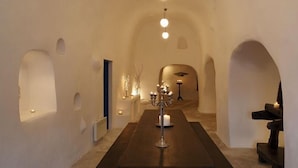 A narrow hallway with white walls and arched doorways, leading to a room with a dark wooden floor and a candelabra.