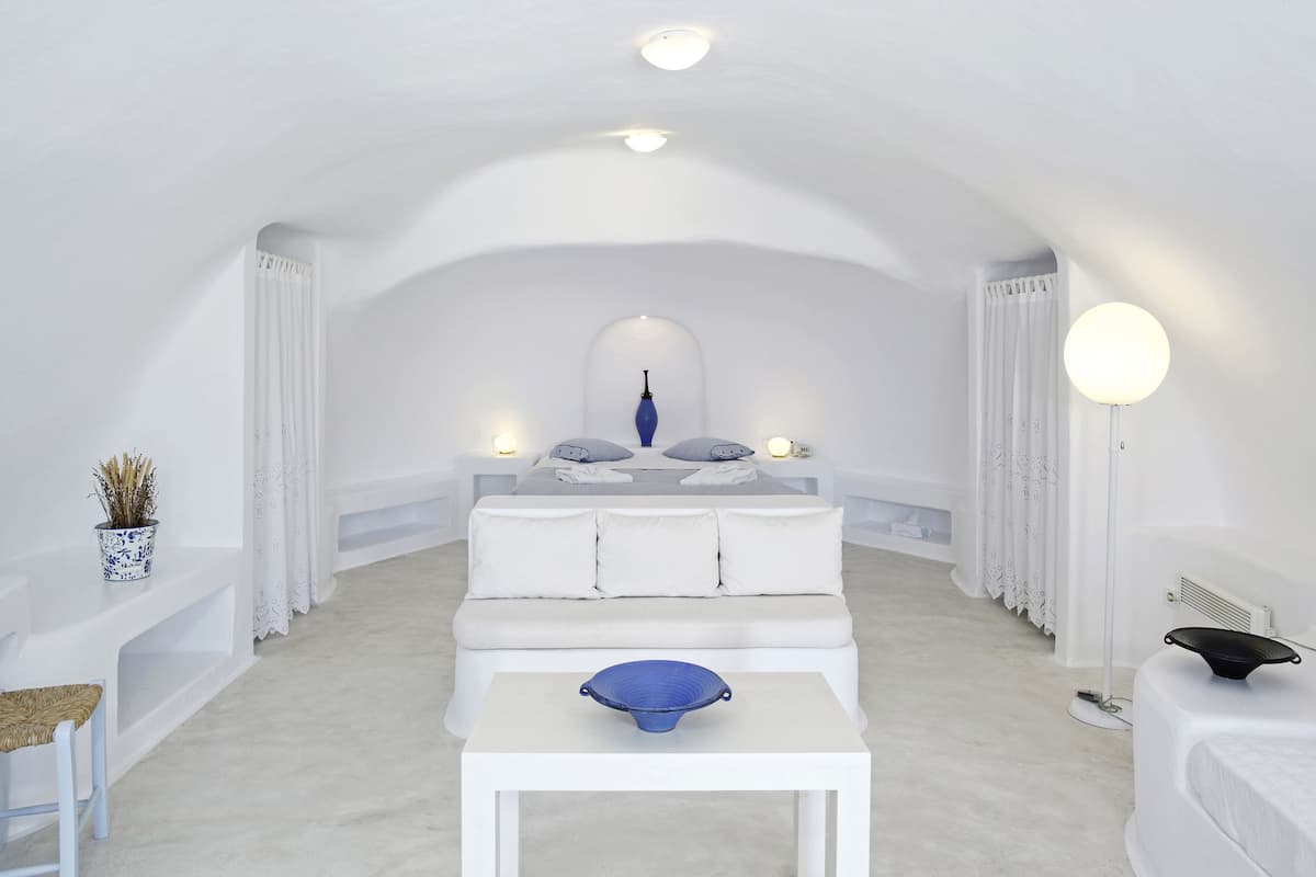 A white, arched room with a bed, bedside table, and a small table with a blue bowl.