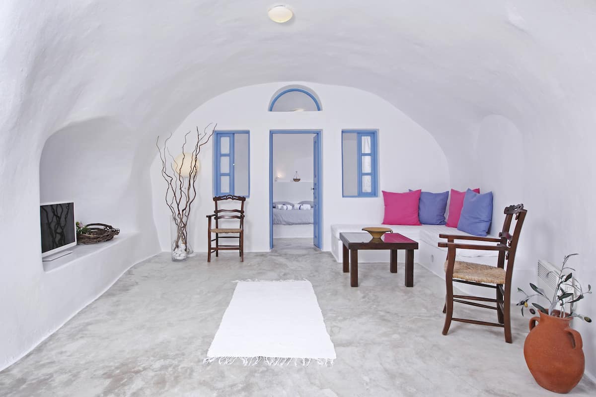 A white-walled room with a sofa, chairs, a TV, and a white rug.