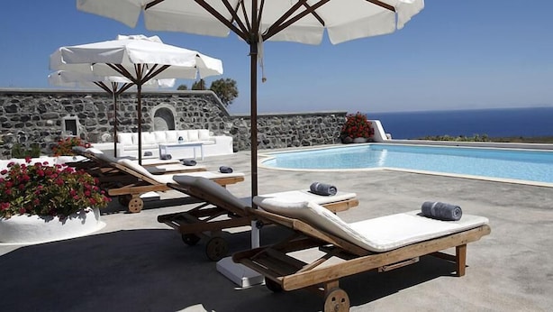 A poolside area with lounge chairs, umbrellas, and a stone wall backdrop.