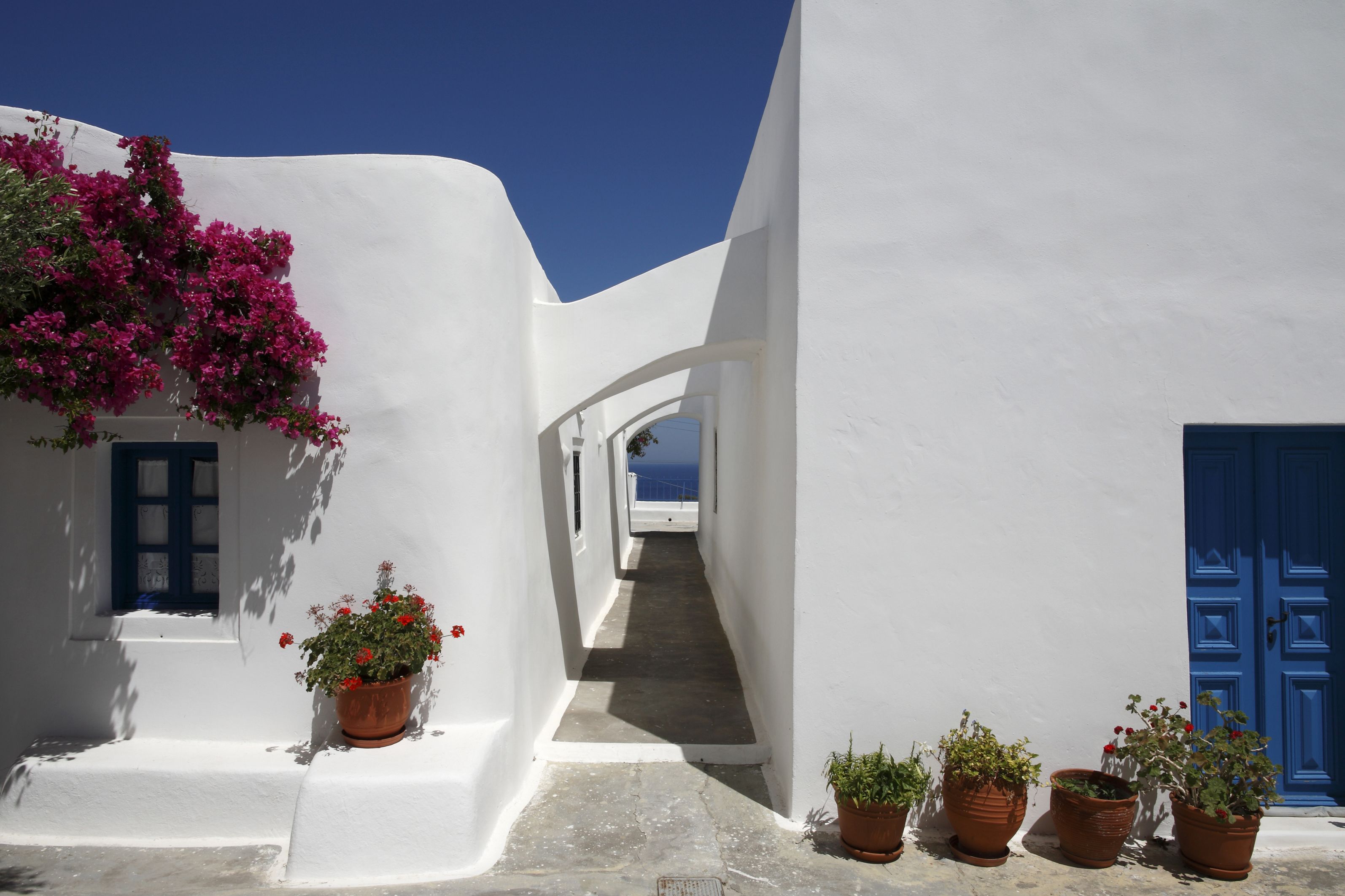 A narrow white-walled street with blue doors and potted plants.