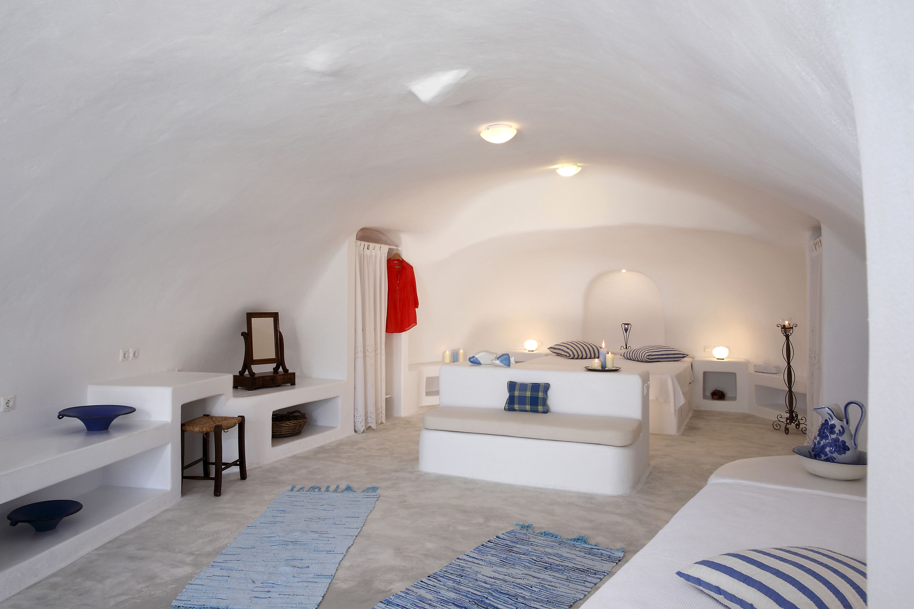 Una habitación moderna y minimalista con paredes blancas y un techo alto. Cuenta con un sofá blanco, una pequeña mesa de madera y una alfombra azul.