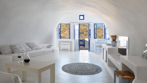 A white interior with a round rug, a sofa, a table with glasses, and a view of the outside.