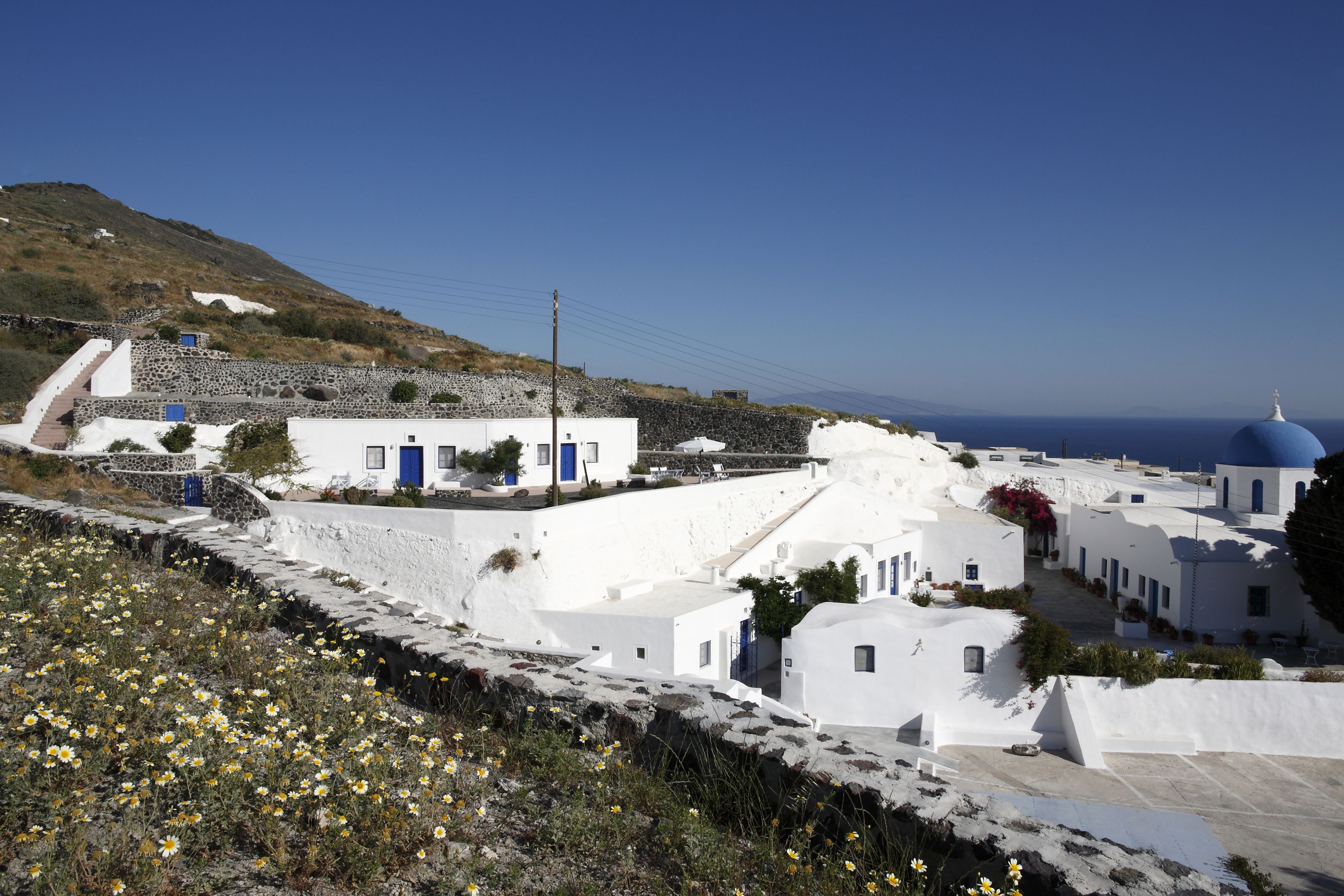 A coastal village with white buildings, a prominent blue dome, and a hillside backdrop.