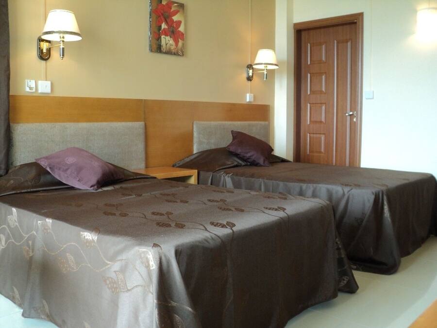 Habitación de hotel con dos camas, cada una con cabecero y almohada. Hay lámparas de pared y una puerta.
