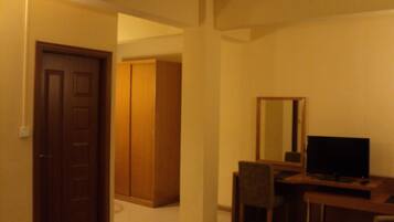 Una habitación con puerta de madera, un armario, un escritorio con silla y un televisor.