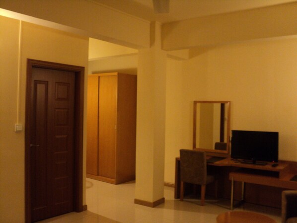 A room with a wooden door, a wardrobe, a desk with a chair, and a television. - Monalysa St Honoré Apartment & Studio (Grand-Baie)