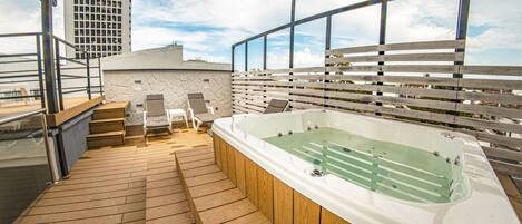 Terraza en la azotea con jacuzzi, piso de madera y vistas a un paisaje urbano.