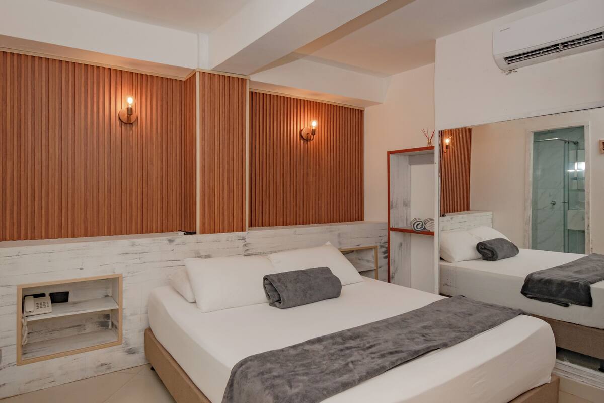 Een moderne hotelkamer met twee bedden, houten lambrisering aan de wanden, een klein nachtkastje met een telefoon en een grote spiegel.