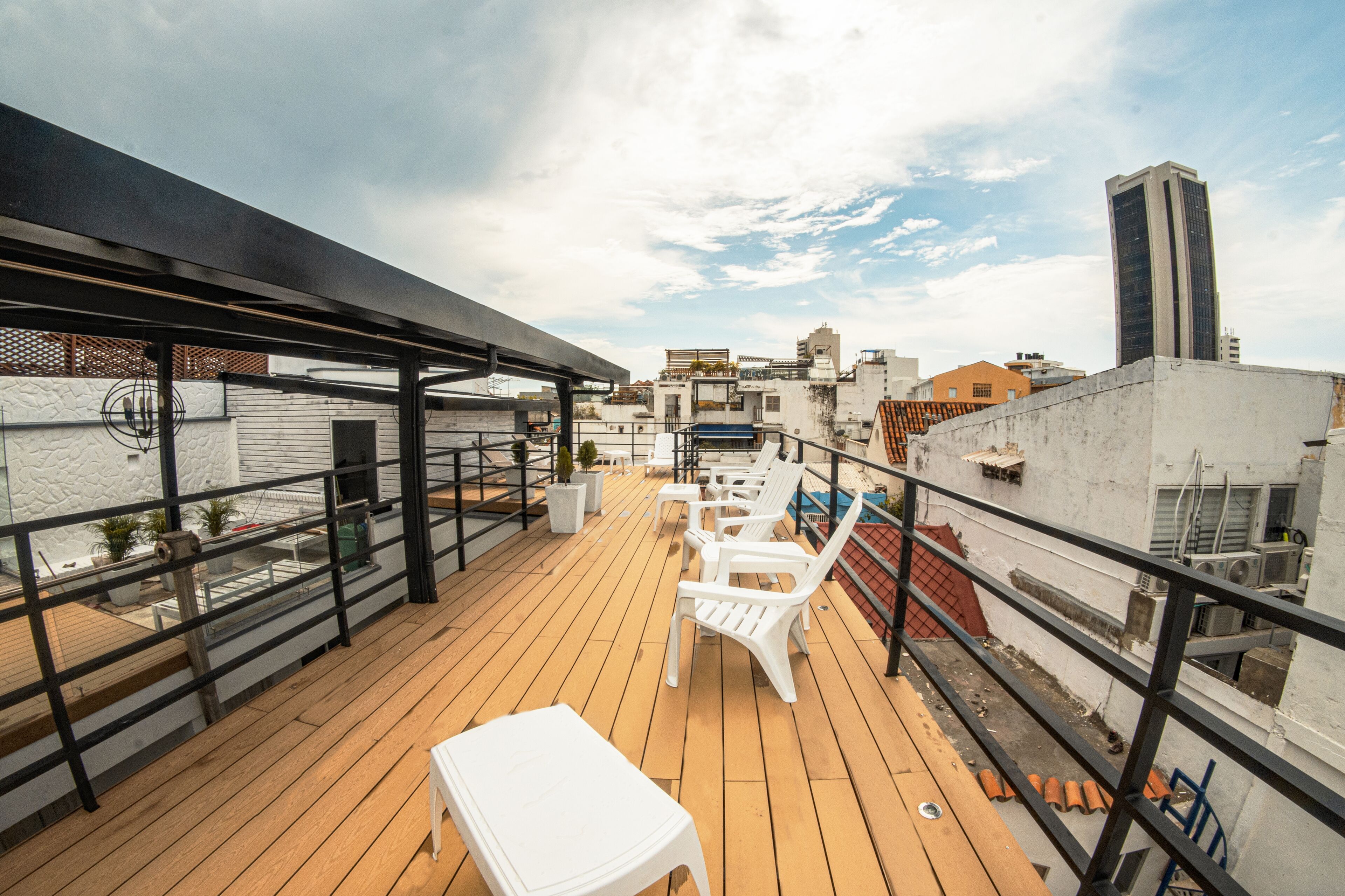 A rooftop terrace with wooden flooring, white plastic chairs, and a white table.