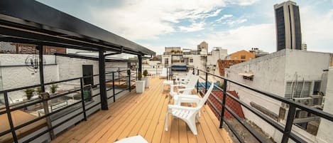 A rooftop terrace with wooden flooring, white plastic chairs, and a white table.