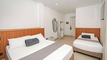 Habitación de hotel con dos camas, cabecero de madera, mesita de noche, espejo y puerta que da a un baño.