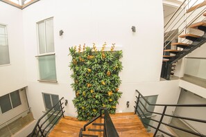 A modern interior with a wooden staircase, a wall-mounted green plant display, and a glass railing.