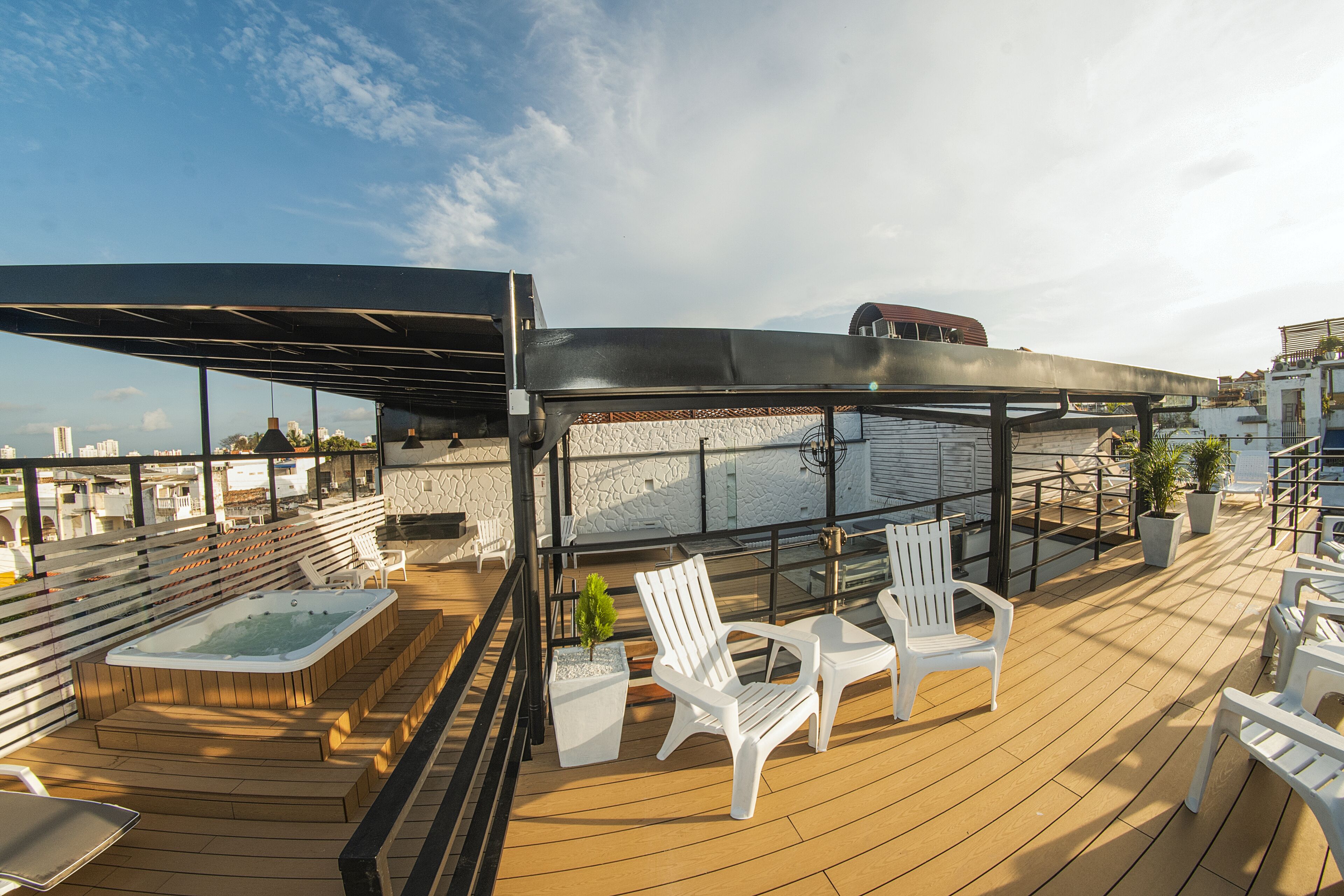 Terraza en la azotea con jacuzzi, sillas blancas y una pérgola.