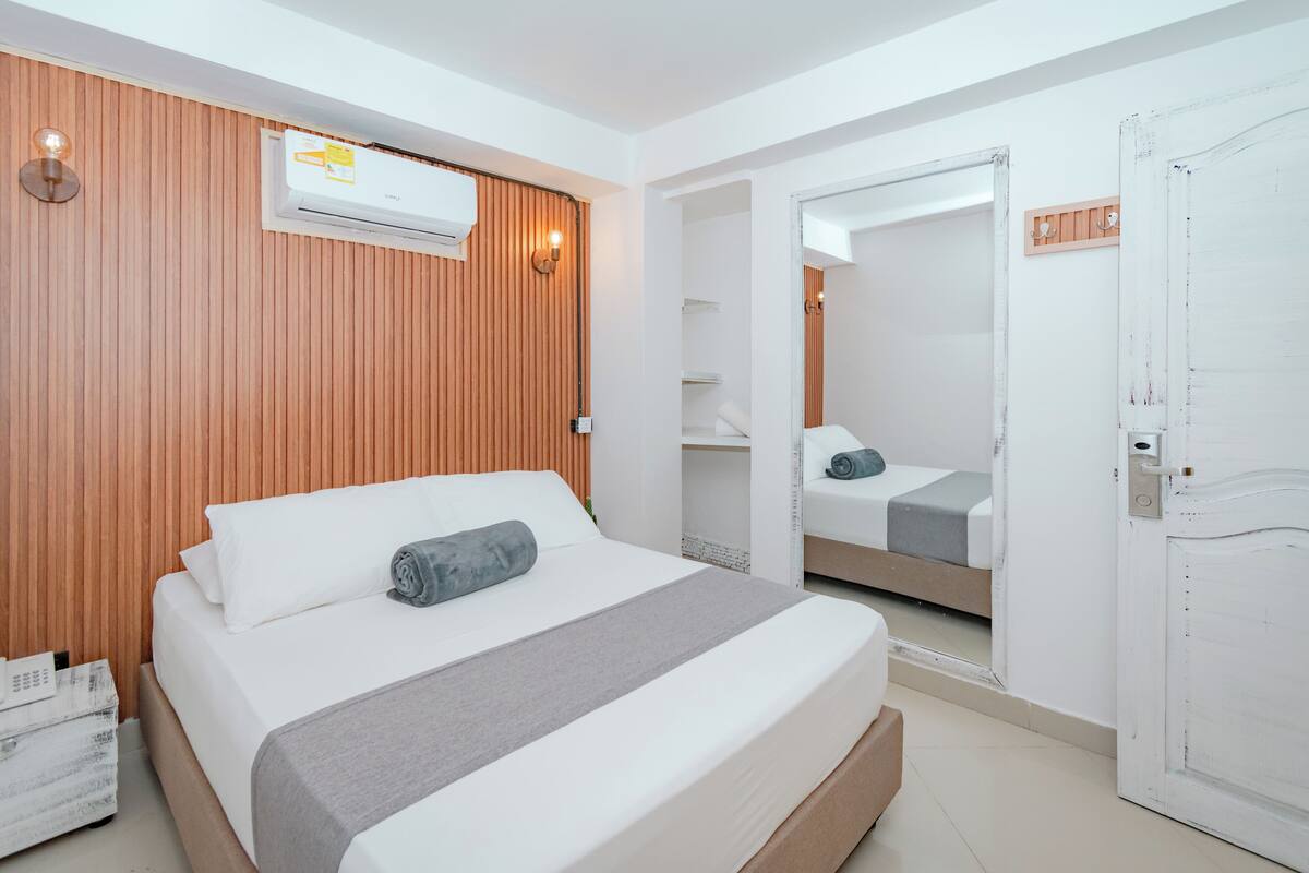 Een moderne hotelkamer met een wand van houten panelen, een groot bed met wit beddengoed, een spiegel en een witte deur.