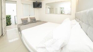 Een slaapkamer met een groot bed, een flatscreen televisie aan de muur en een spiegel boven het bed.