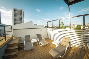 A rooftop deck with wooden flooring, white railings, and two lounge chairs.