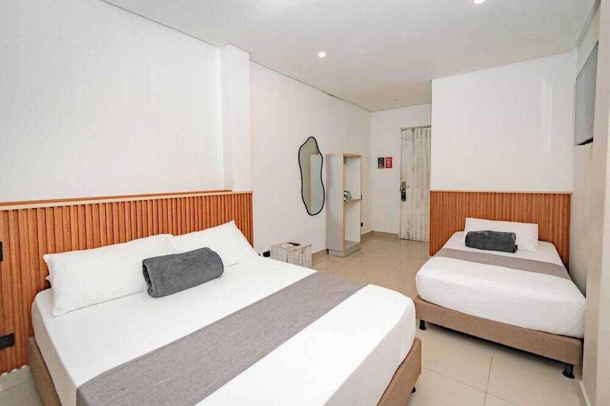 Een hotelkamer met twee bedden, een houten hoofdeinde, een nachtkastje, een spiegel en een deur die naar een andere kamer leidt.