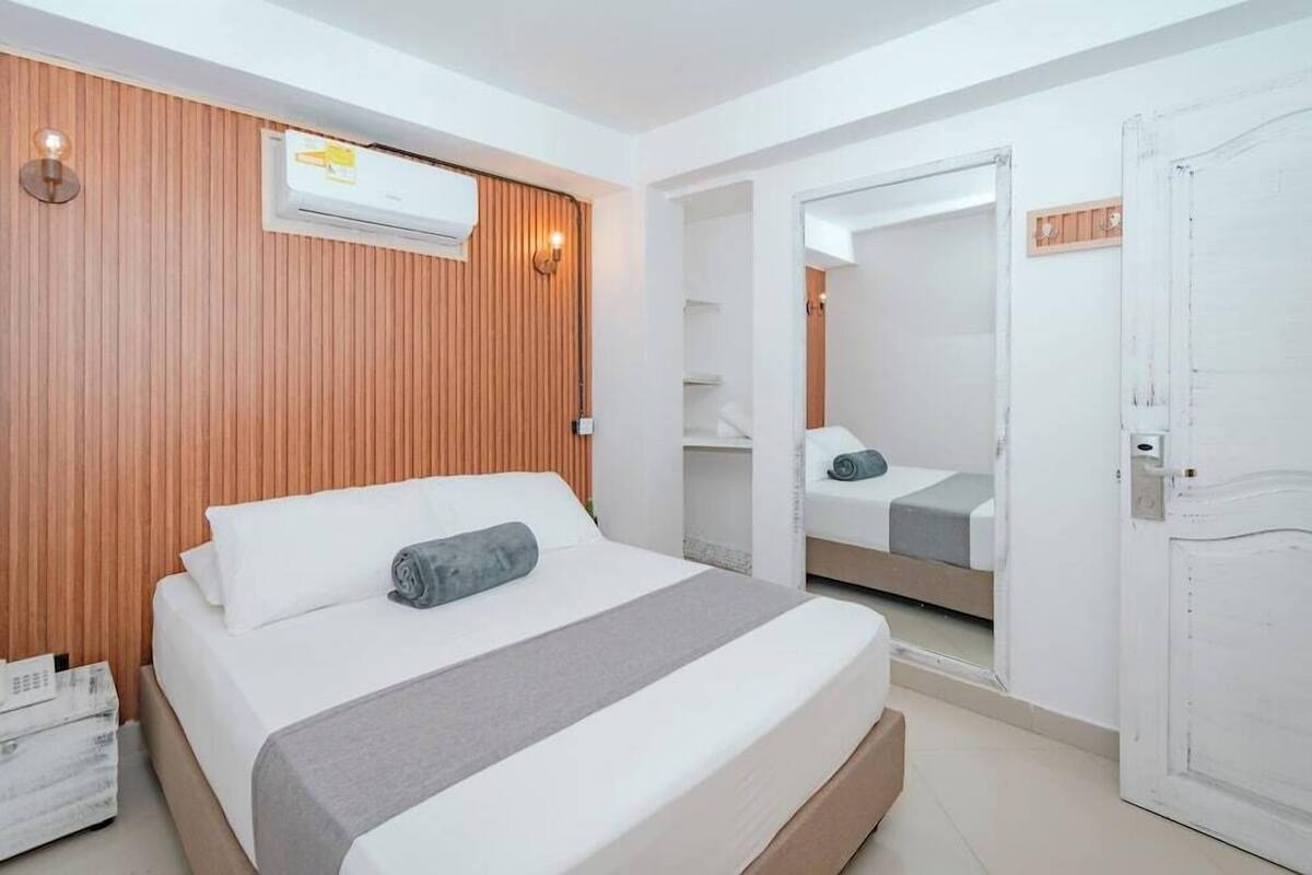 Hotelkamer met een bed, een houten paneelwand, een airconditioner, een spiegel en een witte deur.
