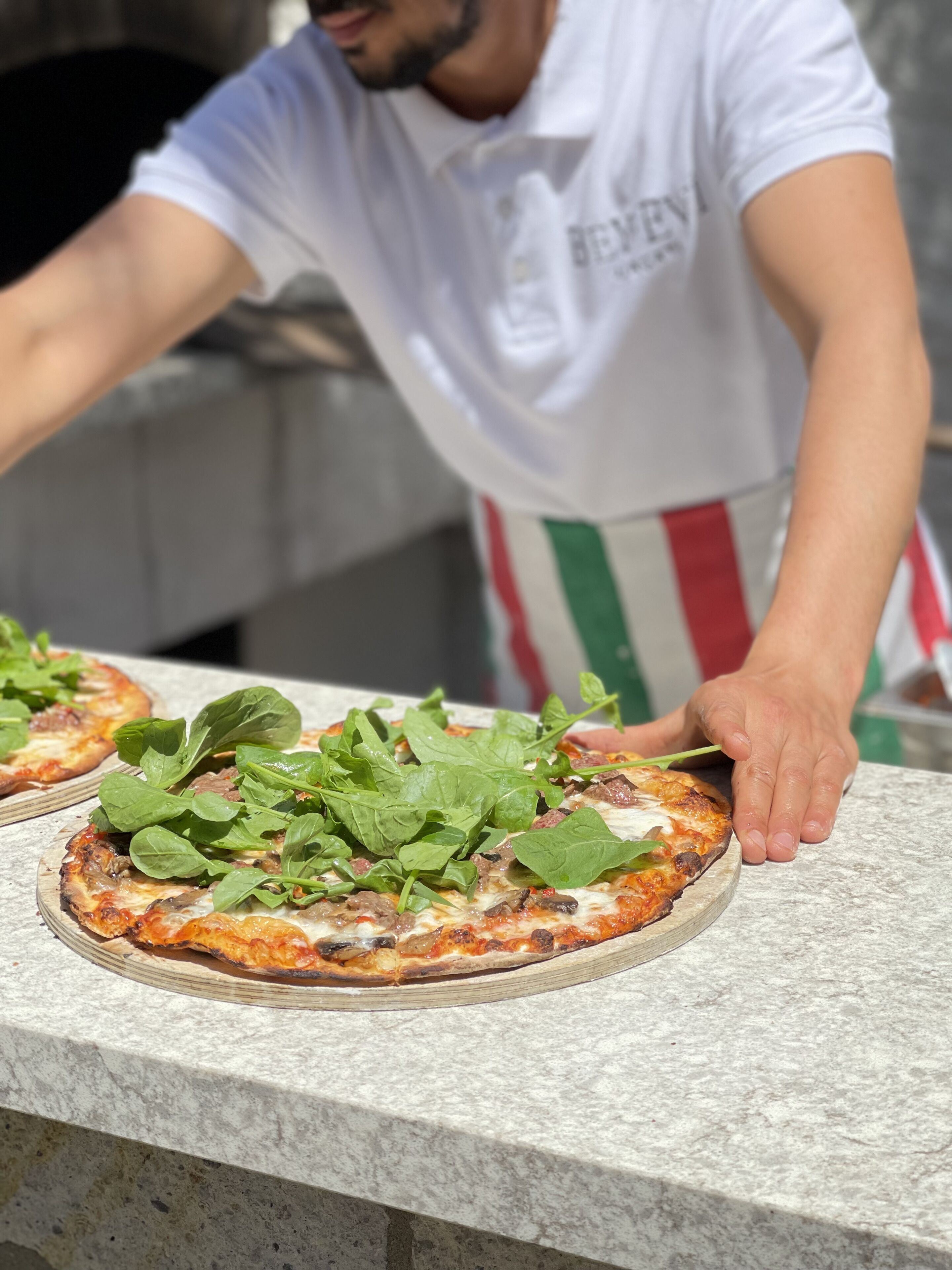 A chef preparing pizzas with fresh greens on a stone countertop.