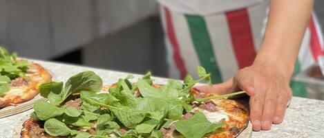 A chef preparing pizzas with fresh greens on a stone countertop.