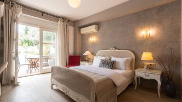 A bedroom with a large bed, a nightstand with a lamp, a vase with branches, and a view of the outside through a glass door.