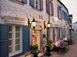 A building with a stone facade, a sign reading "OTEL," and outdoor seating with tables and chairs.