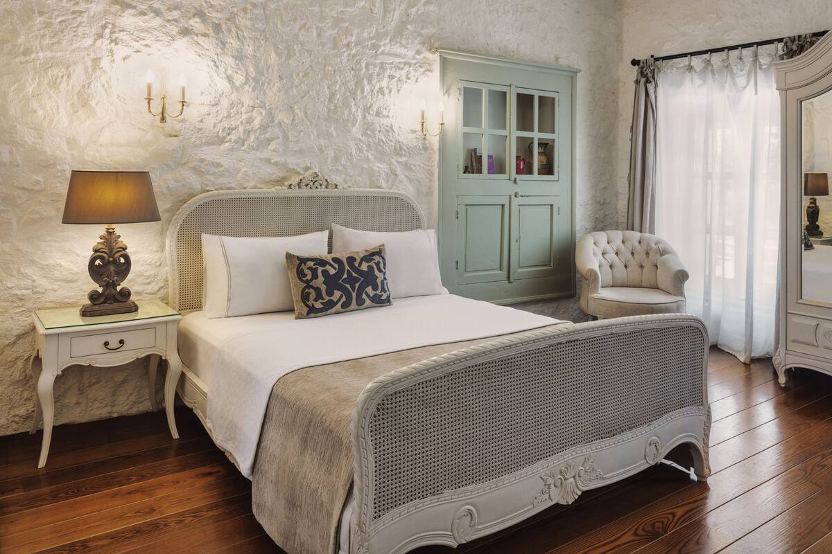 A bedroom with a bed, nightstand, lamp, chair, and a door with glass panels.