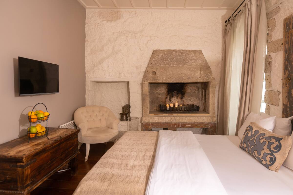A bedroom with a stone fireplace, a bed, a chair, a TV, and a fruit basket.