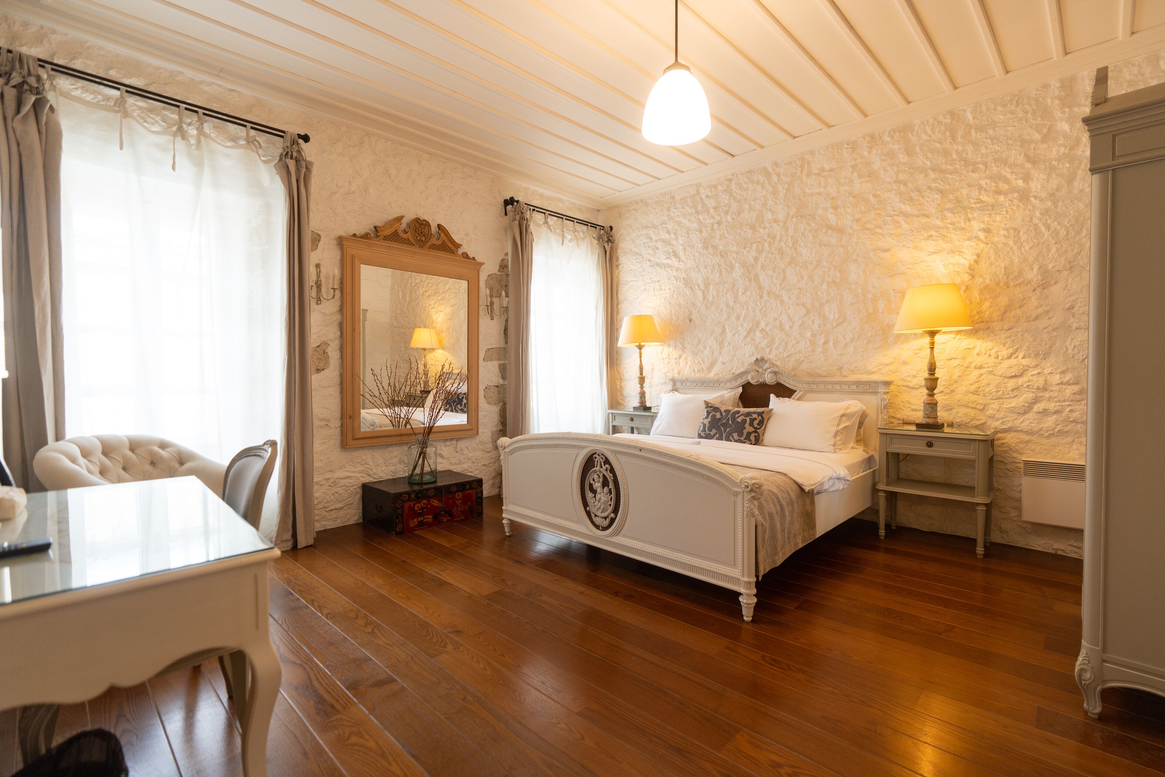 A bedroom with a large bed, a bedside table with a lamp, a chair, and a desk.