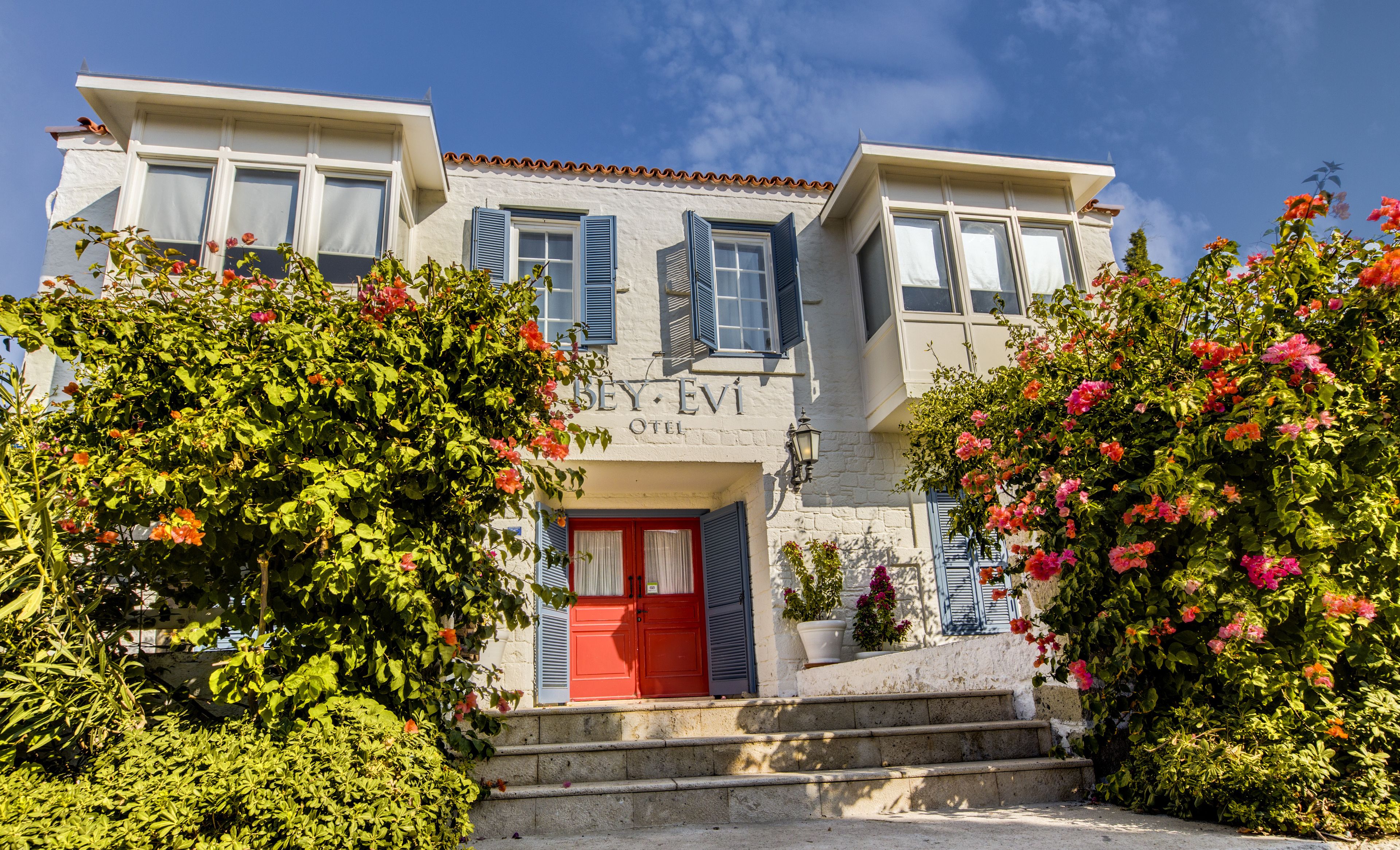 A two-story building with a red door and blue shutters, labeled "BEY-EVI HOTEL".