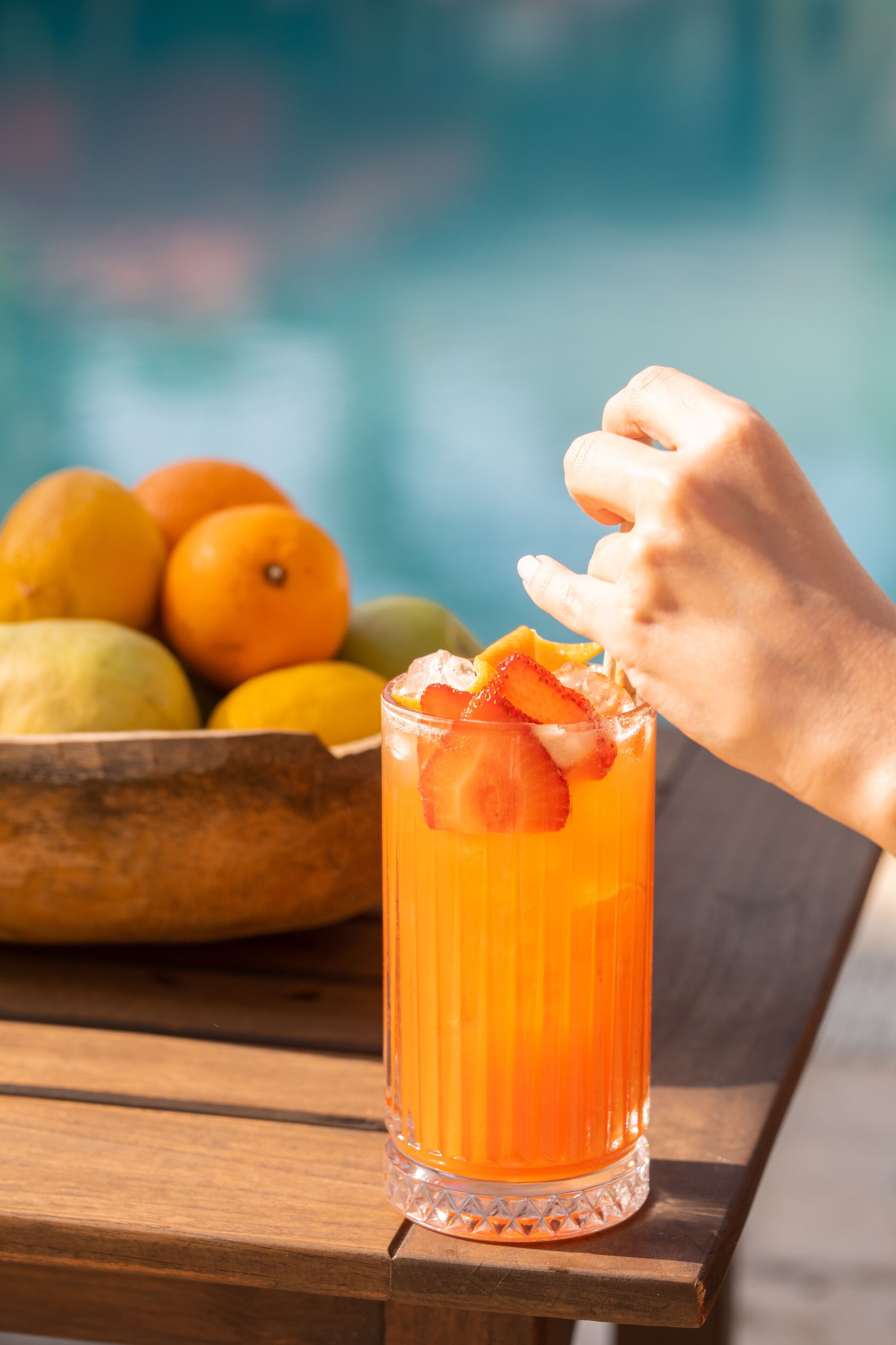 Un got alt amb una beguda de fruita, una mà que s'hi allunya i un bol de fruites al fons.
