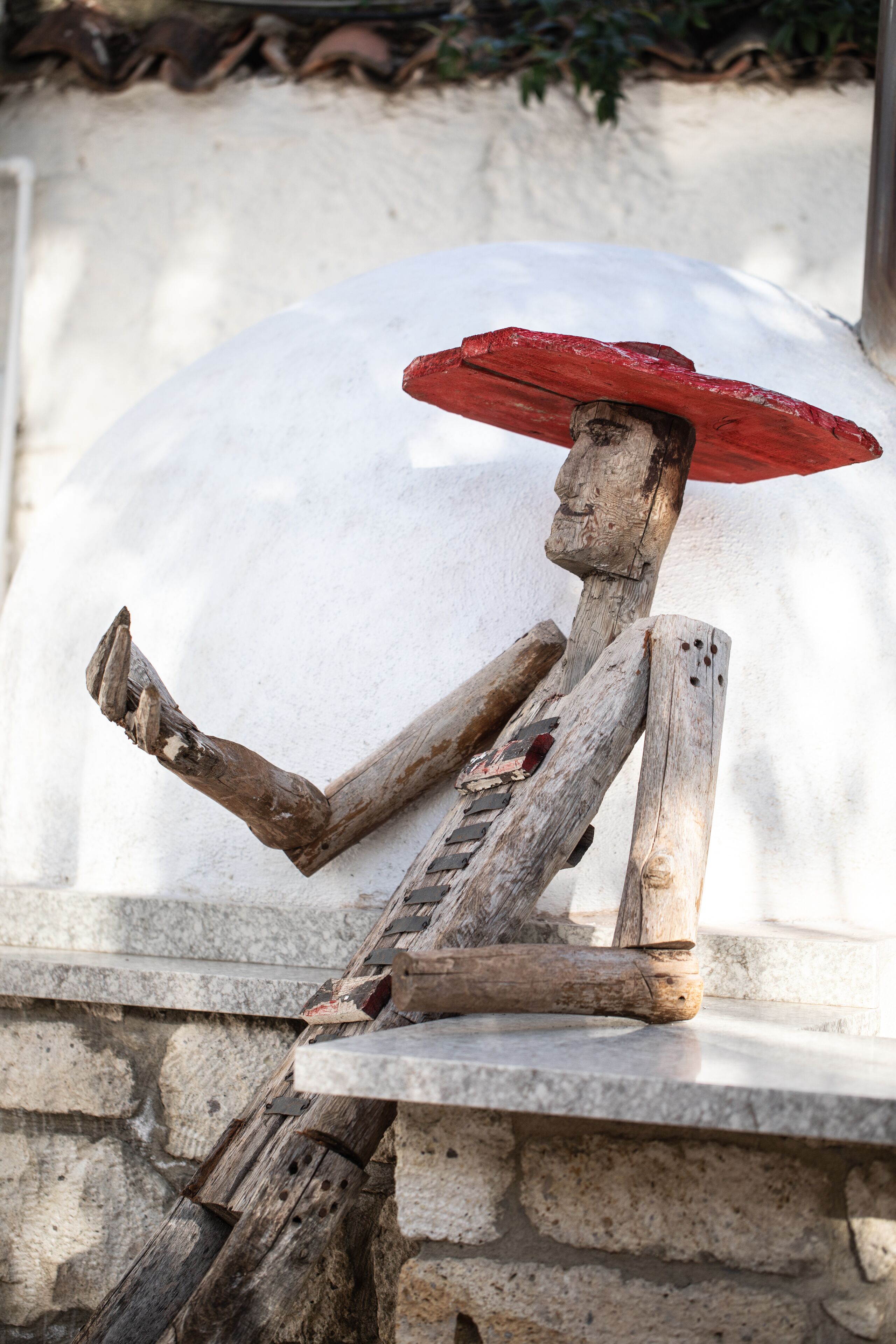 A sculpture of a figure with a red hat sitting on a stone ledge.