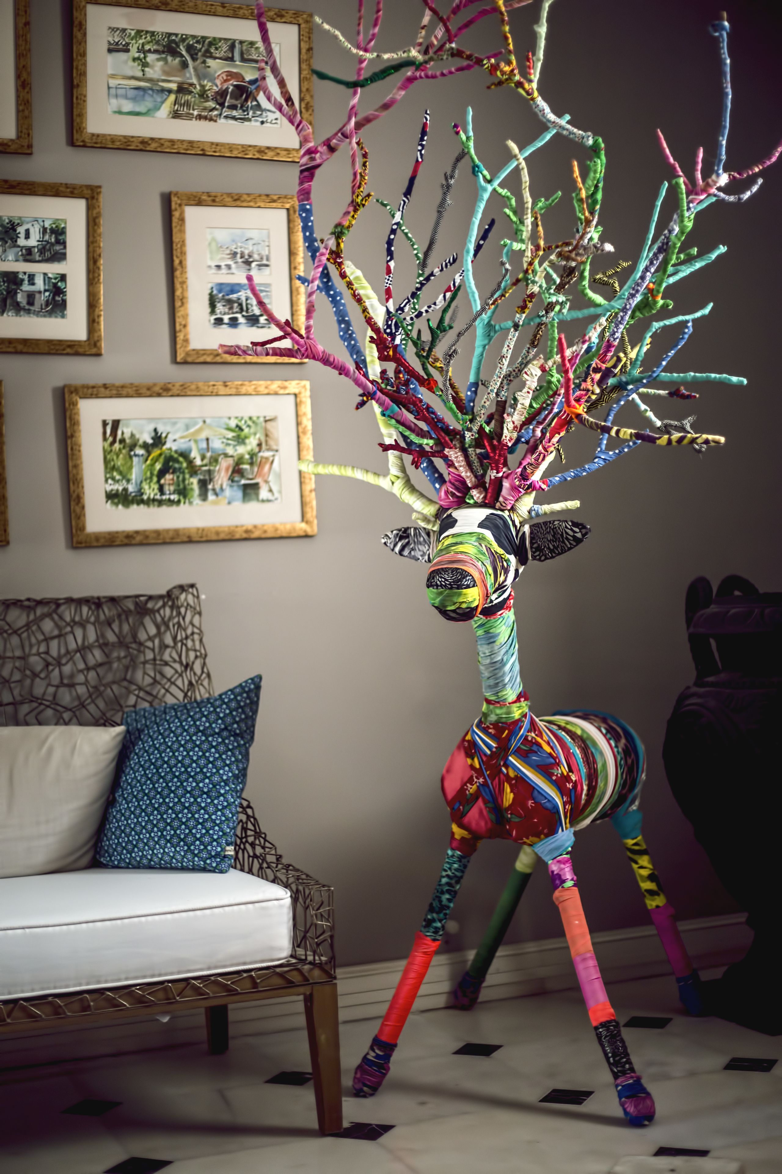 A zebra sculpture with colorful branches in a room with framed pictures on the wall.