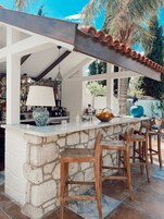 An outdoor bar area with stone walls, wooden bar stools, and a variety of bar tools and bottles.