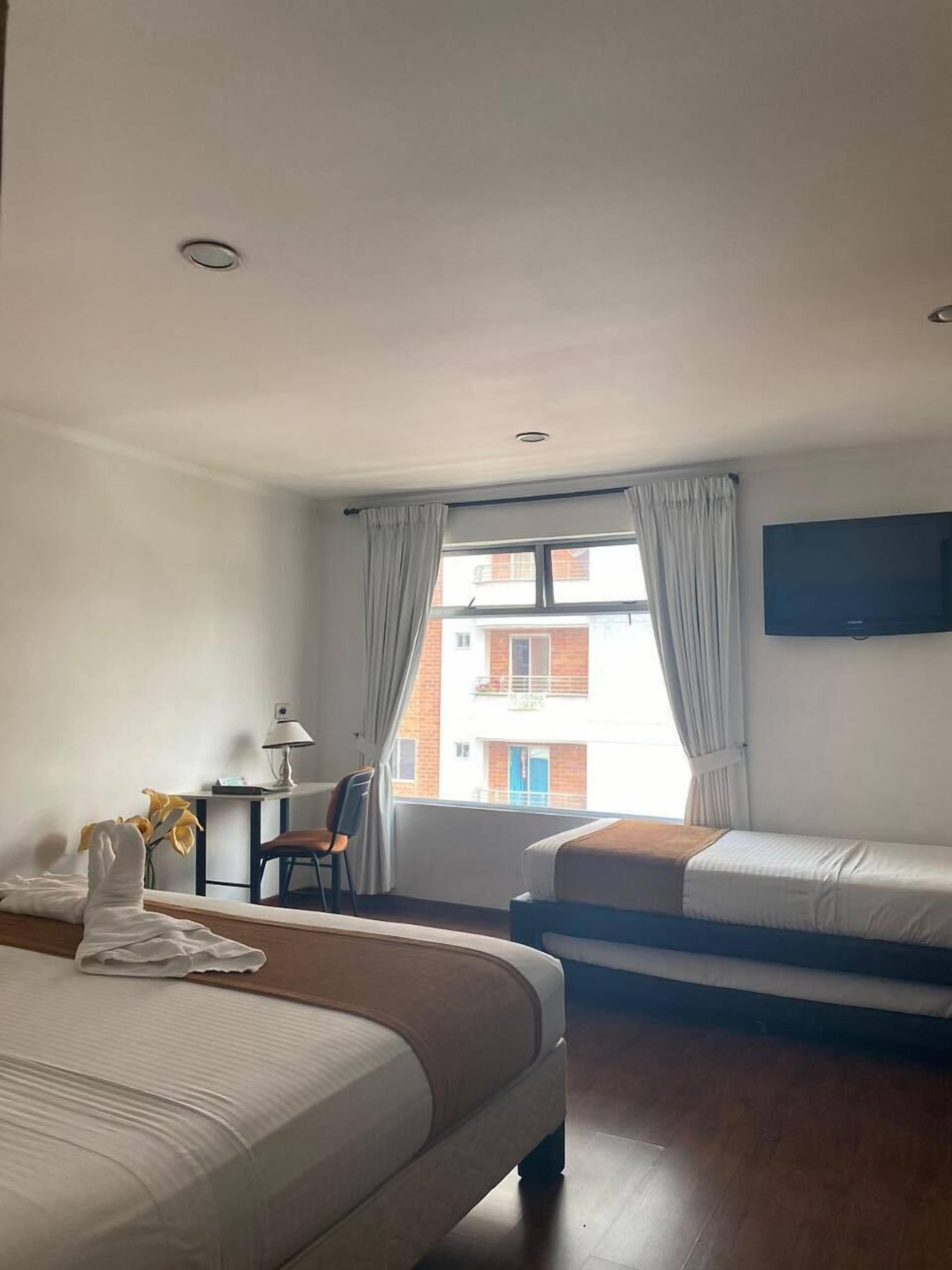 A hotel room with two beds, a desk, a chair, a TV, and a window with curtains.