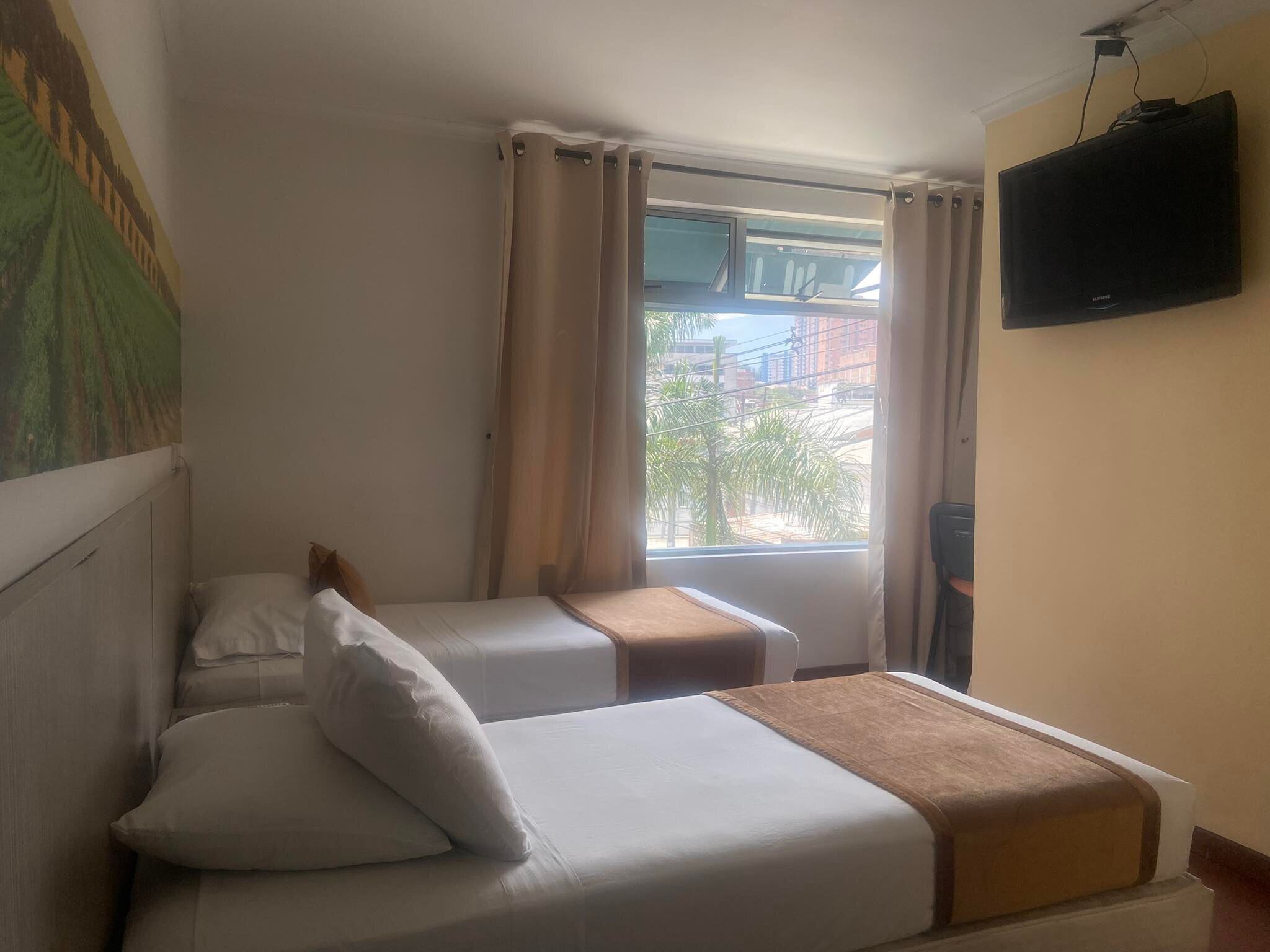 A hotel room with two beds, a TV on the wall, and a window with curtains.