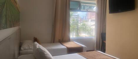 A hotel room with two beds, a TV on the wall, and a window with curtains.