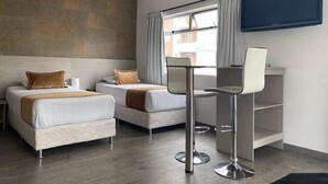 A hotel room with two beds, a desk with a chair, a TV mounted on the wall, and a window with curtains. - Hotel Portón Sabaneta (Sabaneta)