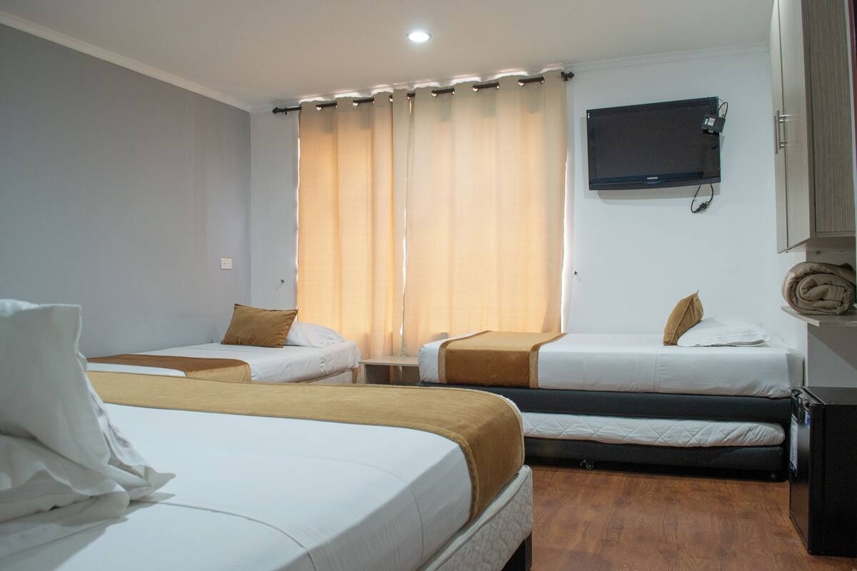 A hotel room with two single beds, a TV mounted on the wall, and a wooden floor.