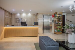 A reception desk with a wooden finish, a vending machine, a refrigerator, and a seating area with a glass table.