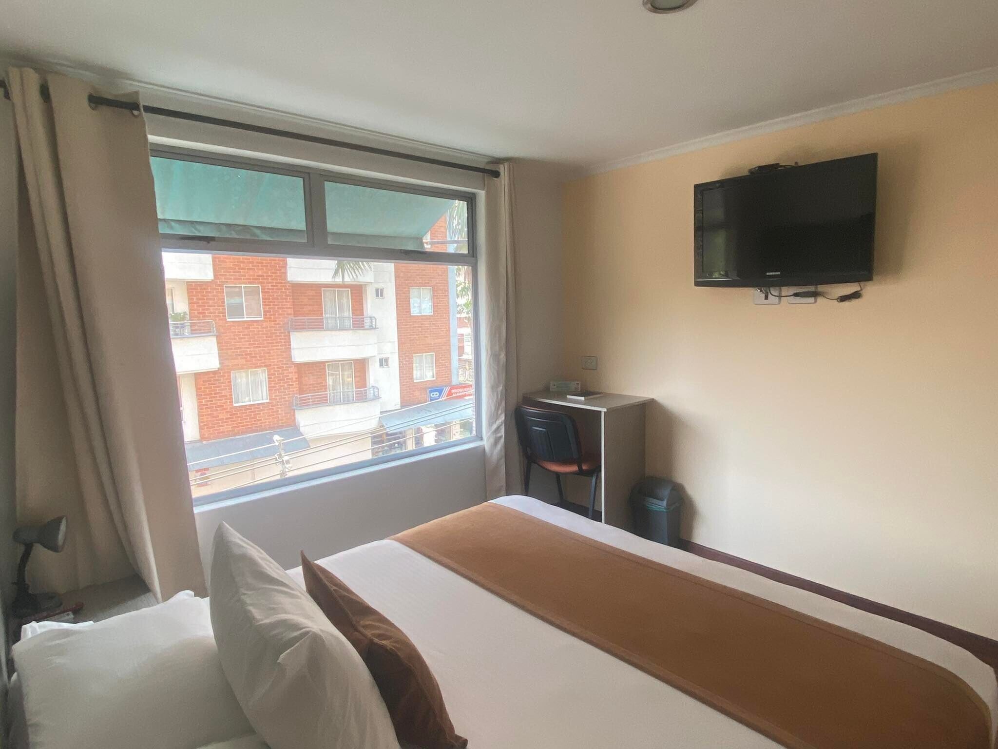 A hotel room with a bed, a desk, a chair, a television, and a window with a view of a building.