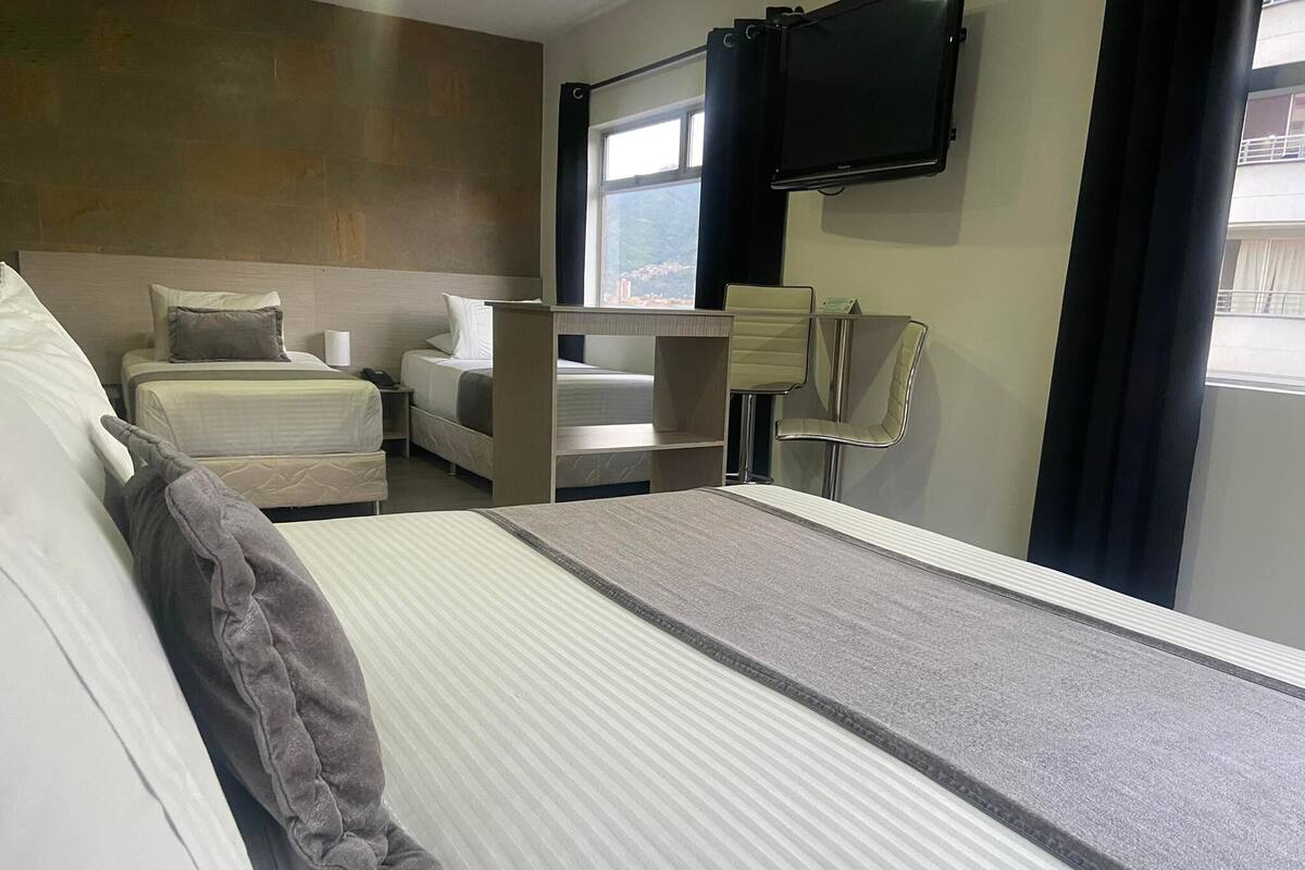 A hotel room with a bed, a desk, a chair, and a TV mounted on the wall.