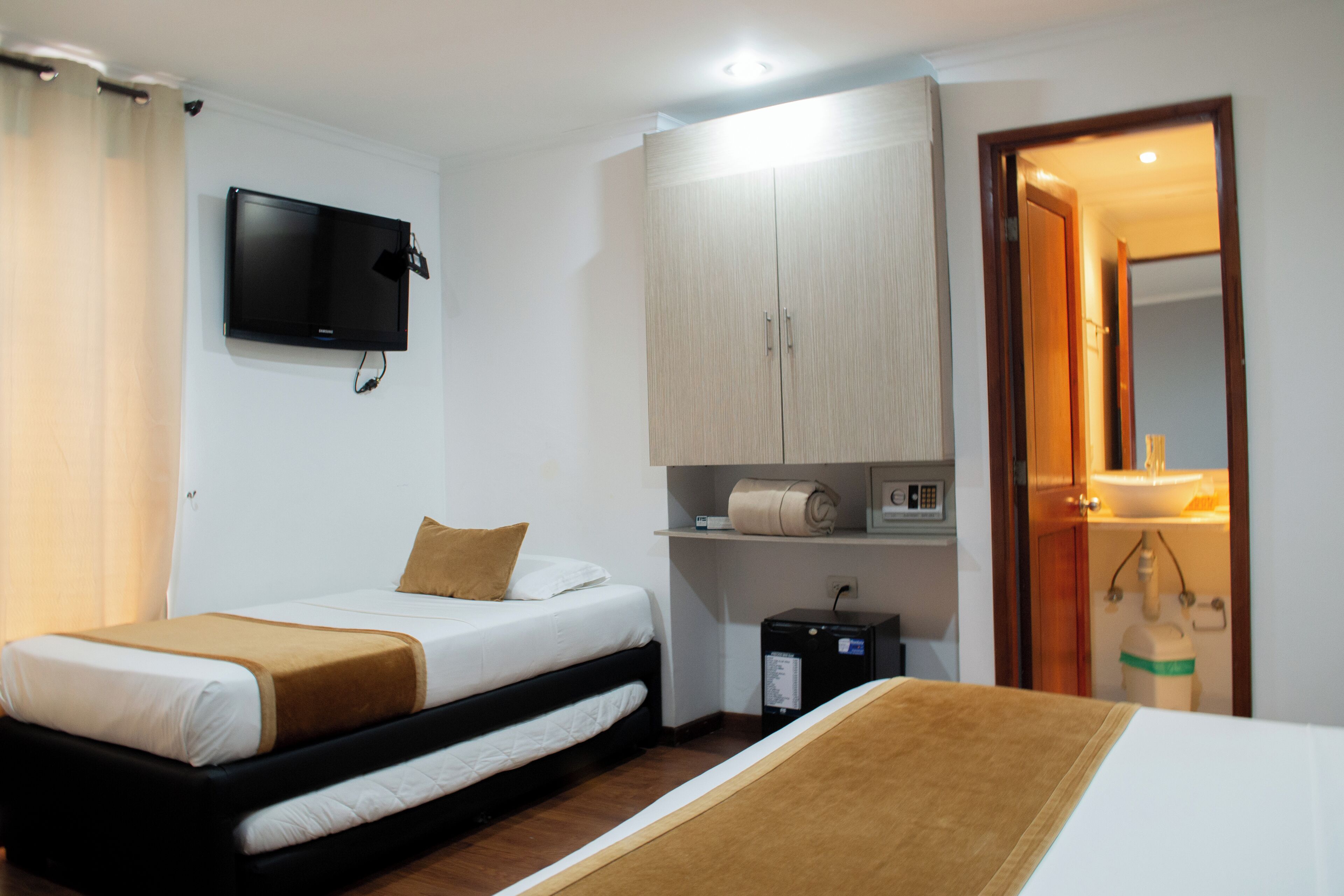 Une chambre d’hôtel avec un lit, un téléviseur fixé au mur, une armoire et une salle de bain visible à travers une porte ouverte.